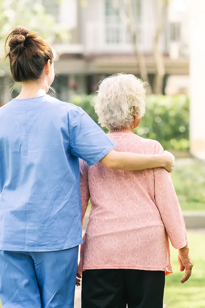 Pflegekraft begleitet Seniorin im Garten